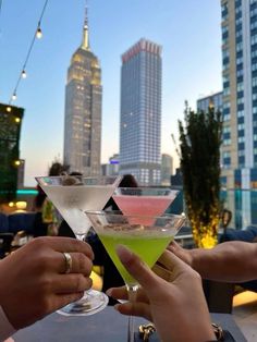 two people toasting with cocktails in front of the city's skyscrapers