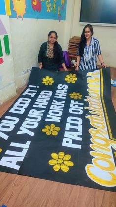 two women standing next to a large banner