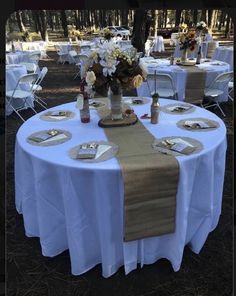 the table is set with white linens and place settings for guests to sit at