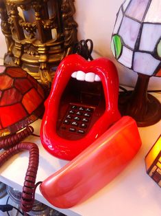 a red telephone sitting on top of a table next to lamps and a lamp shade