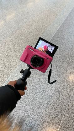 a person holding a camera up to take a picture on the ground with it's pink case