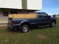 a blue pick up truck parked in front of a white house with a wooden box on the back