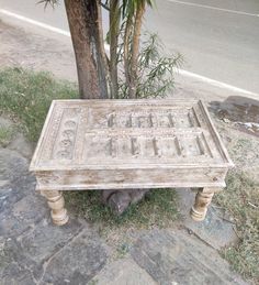 an old wooden bench sitting next to a tree on the side of a road in front of a palm tree