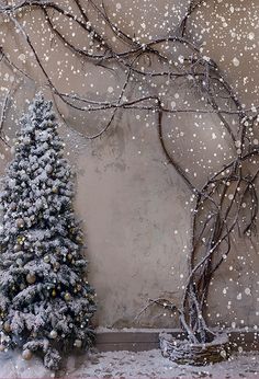 a small christmas tree sitting next to a wall with snow falling on it and branches