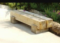 a wooden bench sitting on top of a cement ground next to trees and bushes with purple flowers in the background