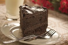 a piece of chocolate cake on a plate with a fork and glass of milk next to it