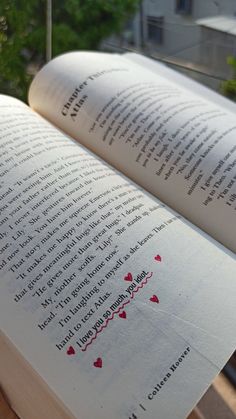 an open book sitting on top of a wooden table next to a window sill