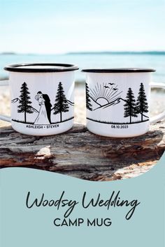 two coffee mugs sitting on top of a wooden table next to the ocean and trees