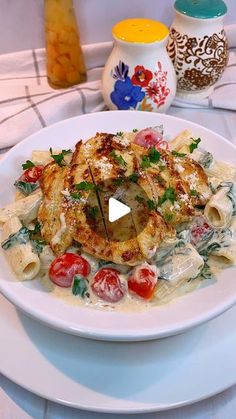 a white plate topped with pasta and meat covered in sauce next to two vases