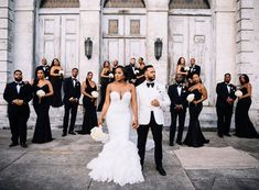 a bride and groom standing in front of a large group of people wearing tuxedos