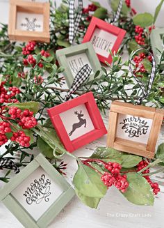 christmas decorations with red berries and green leaves on the table, including small frames that say merry