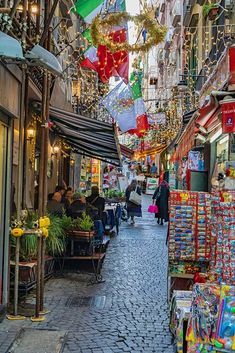 people are walking down an alley way with christmas decorations hanging from the ceiling and shops on either side