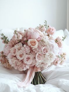 a bridal bouquet on a bed with white sheets and pink flowers in the background