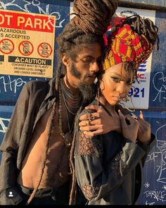 a man and woman standing next to each other in front of a wall with graffiti on it