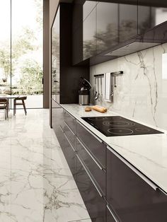 a modern kitchen with marble counter tops and black cabinets, along with a dining table in the background