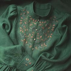 a green dress with embroidered flowers on the chest and collar, sitting on top of a bed