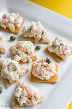 small crackers topped with crab salad and capers on a white plate next to an orange napkin