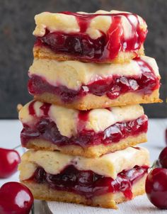 cherry cheesecake bars stacked on top of each other with fresh cherries in the background