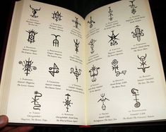 an open book with symbols on it in someone's hand and the pages are black