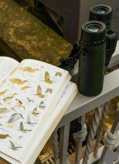 two binoculars sitting on top of an open book next to a pair of binoculars laying on a railing