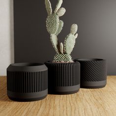 three black planters sitting on top of a wooden table next to each other and one has a cactus in it