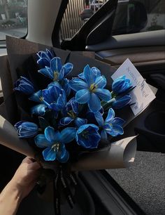 a bouquet of blue flowers sitting in the passenger seat of a car, being held by someone's hand