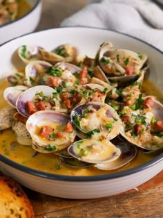 a bowl filled with clams and sauce on top of a wooden table next to bread