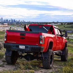 a red pick up truck parked on top of a grass covered field next to a city