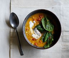 a bowl of soup with spinach, cheese and other toppings on the side