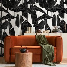 an orange couch in front of a black and white wallpaper with leaves on it