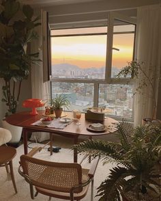 a living room filled with furniture and a large window overlooking the cityscape at sunset