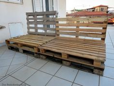 a bed made out of wooden pallets sitting on top of a tiled floor next to a building