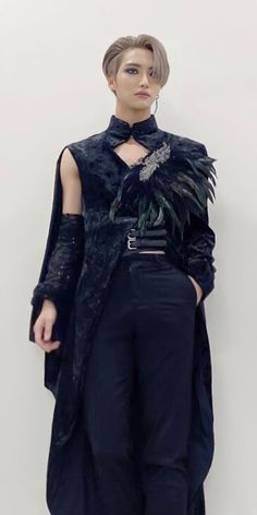 a woman standing in front of a white wall wearing a black outfit with feathers on it