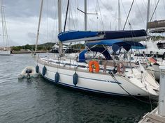 a sailboat docked at a dock with other boats in the water and one is blue and white