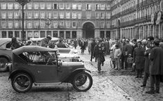 an old car is parked in the middle of a crowded street with people standing around it