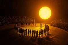 a large group of people standing in front of a giant yellow ball on a stage