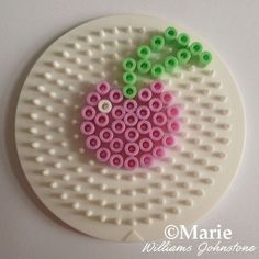 a piece of art made out of legos on top of a white plate with green and pink beads