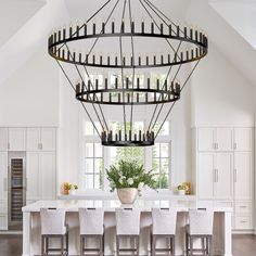 a large chandelier hanging from the ceiling in a kitchen with white cabinets and chairs