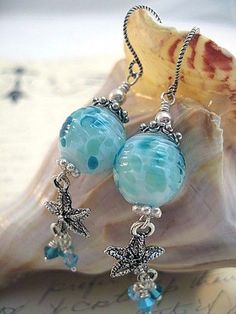 two blue glass beads are hanging from a silver ear chain on a seashell with a sea shell in the background