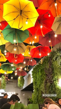 many colorful umbrellas are hanging from the ceiling above tables in a restaurant or bar