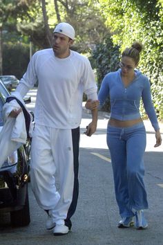 the man and woman are walking down the street with their car door open, holding hands