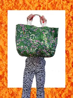 a woman holding a large green bag over her head with flowers on it and an orange background