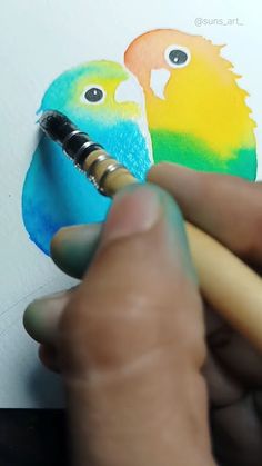 a person is drawing two birds on a piece of paper with colored pencils in their hands