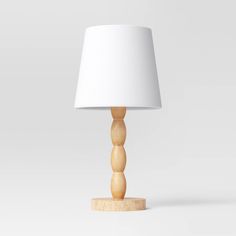 a wooden table lamp with a white shade on the top and bottom, in front of a light gray background