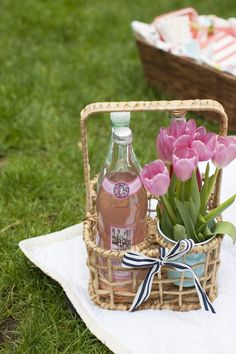 pink flowers in a wicker basket next to a bottle of booze on a towel