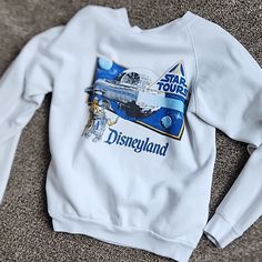 a white sweatshirt with the words disneyland printed on it and a star tours logo in blue