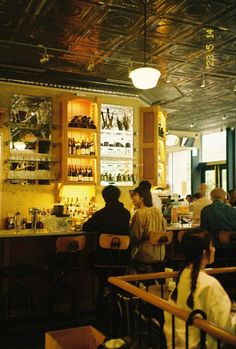 people sitting at tables in a restaurant with many bottles on the wall and shelves behind them