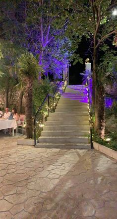 an outdoor dining area with steps leading up to the stairs and lit trees at night