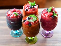 three glasses filled with different types of drinks on top of a wooden table next to each other