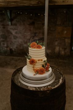 a white wedding cake with orange flowers on top sits on a barrel at the reception